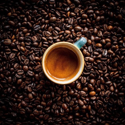 Top view of a cup of espresso surrounded by dark roasted coffee beans illustrating coffee vs espresso difference